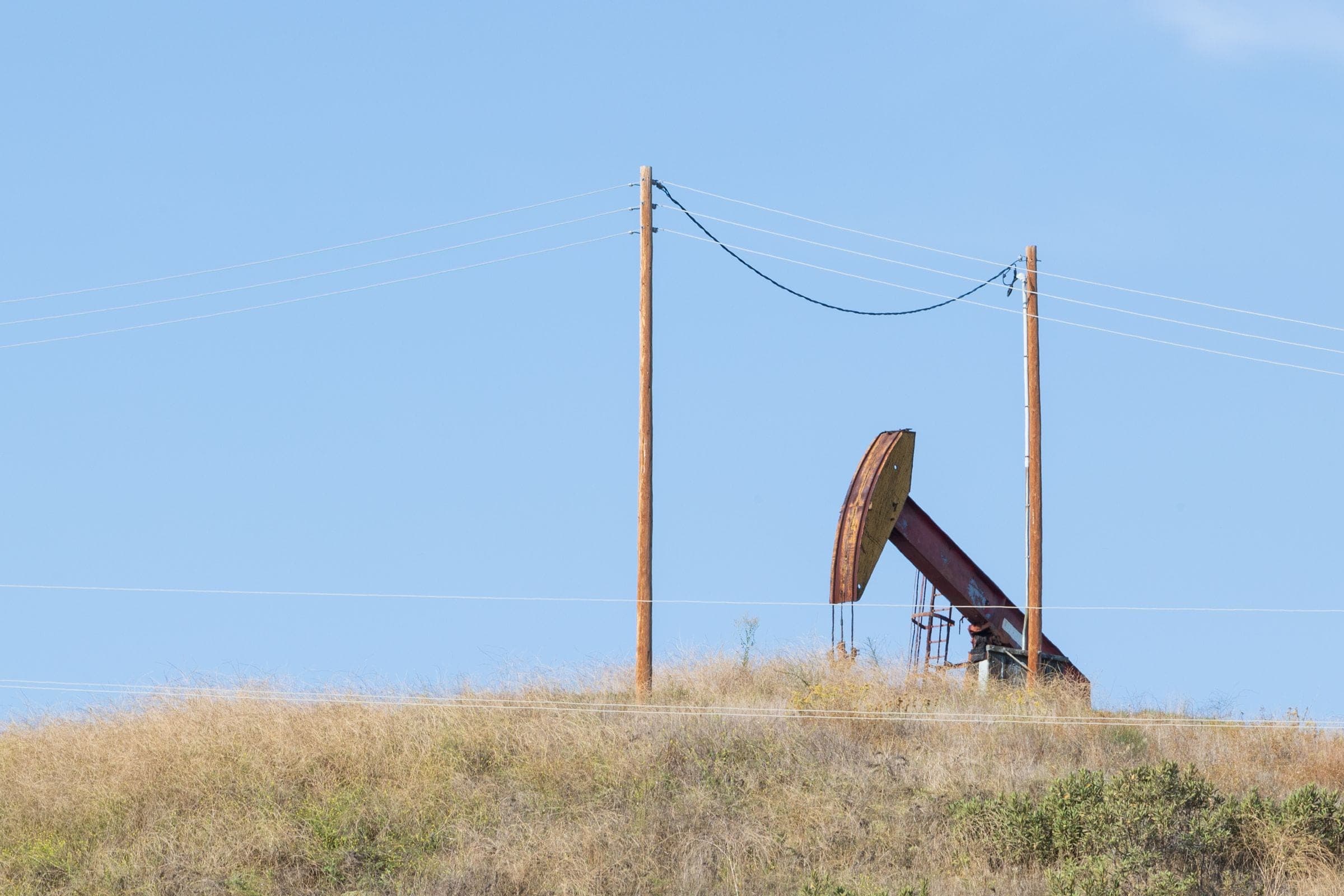 An oil pumpjack and power poles on a dry rise in the West Odessa countryside