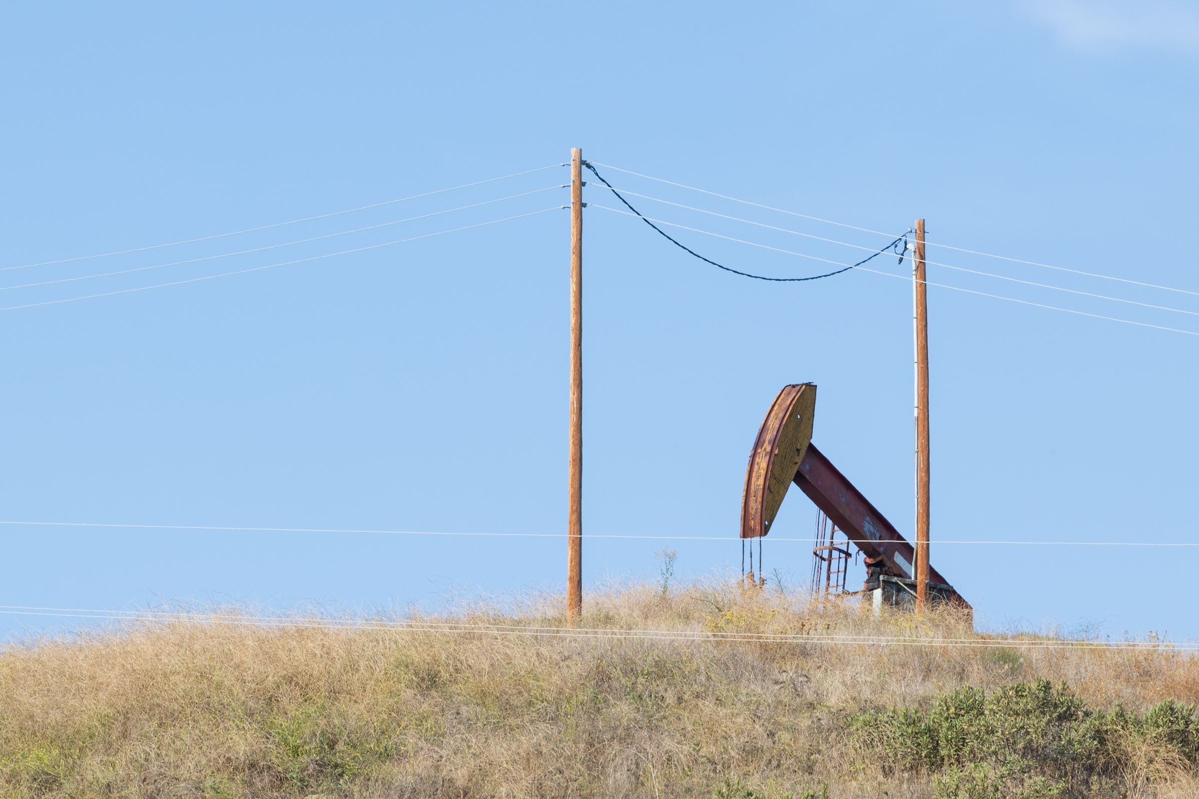 An oil pumpjack and power poles on a dry rise in the West Odessa countryside